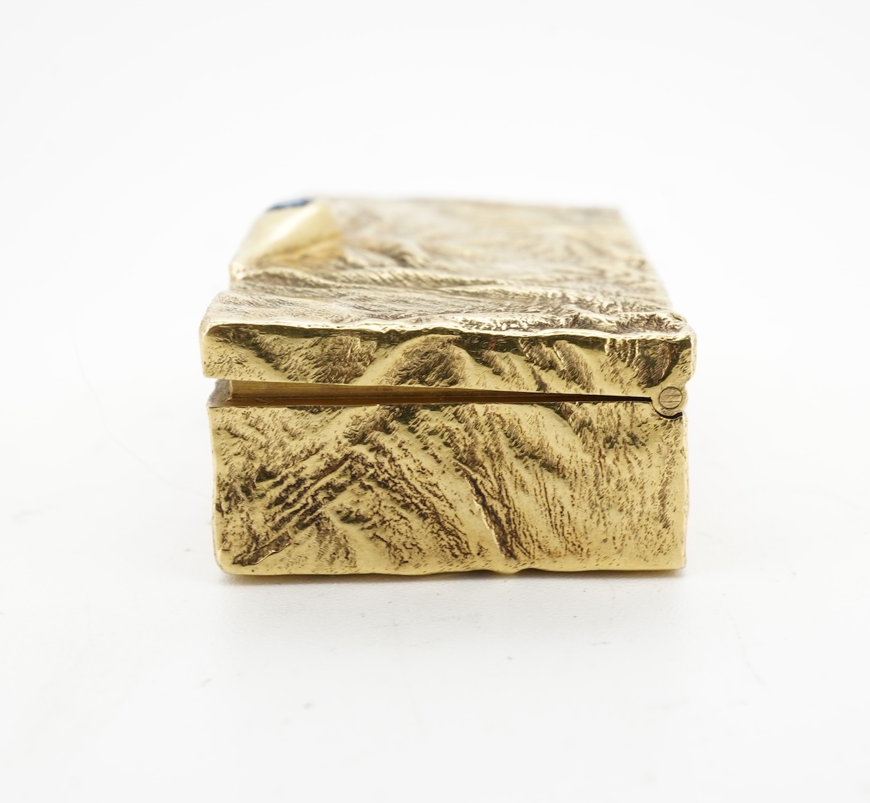 Dunhill, an attractive 9ct gold and sapphire snuffbox, circa 1973, the rectangular box of samorodok finish, the hinged lid set with a foil-backed oval sapphire, measuring approximately 5.1 x 2.7 x 1.6cm, signed Dunhill L